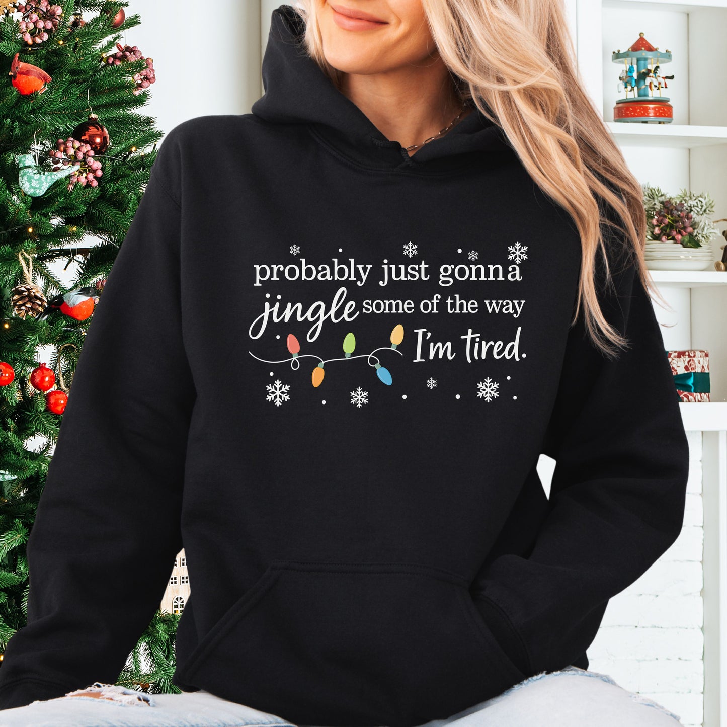 Person wearing black hoodie with Christmas lights and the text "probably just gonna jingle some of the way. I'm tired".
