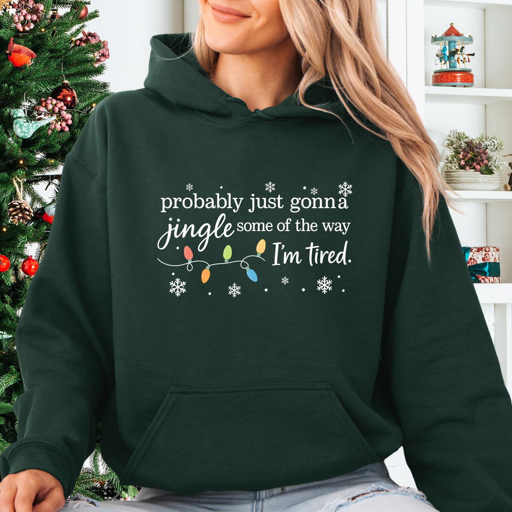 Person wearing forest green hoodie with Christmas lights and the text "probably just gonna jingle some of the way. I'm tired".