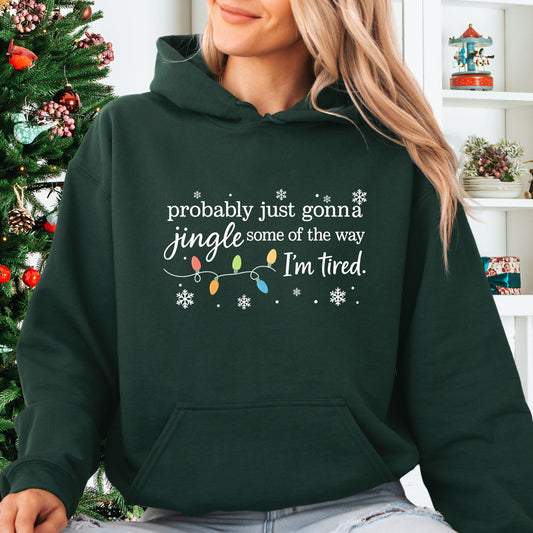 Person wearing forest green hoodie with Christmas lights and the text "probably just gonna jingle some of the way. I'm tired".