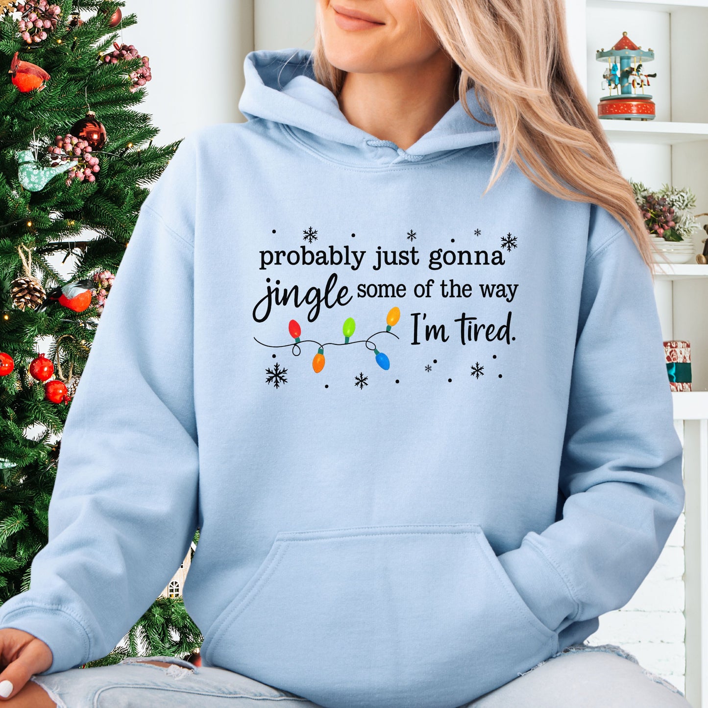 Person wearing light blue hoodie with Christmas lights and the text "probably just gonna jingle some of the way. I'm tired".