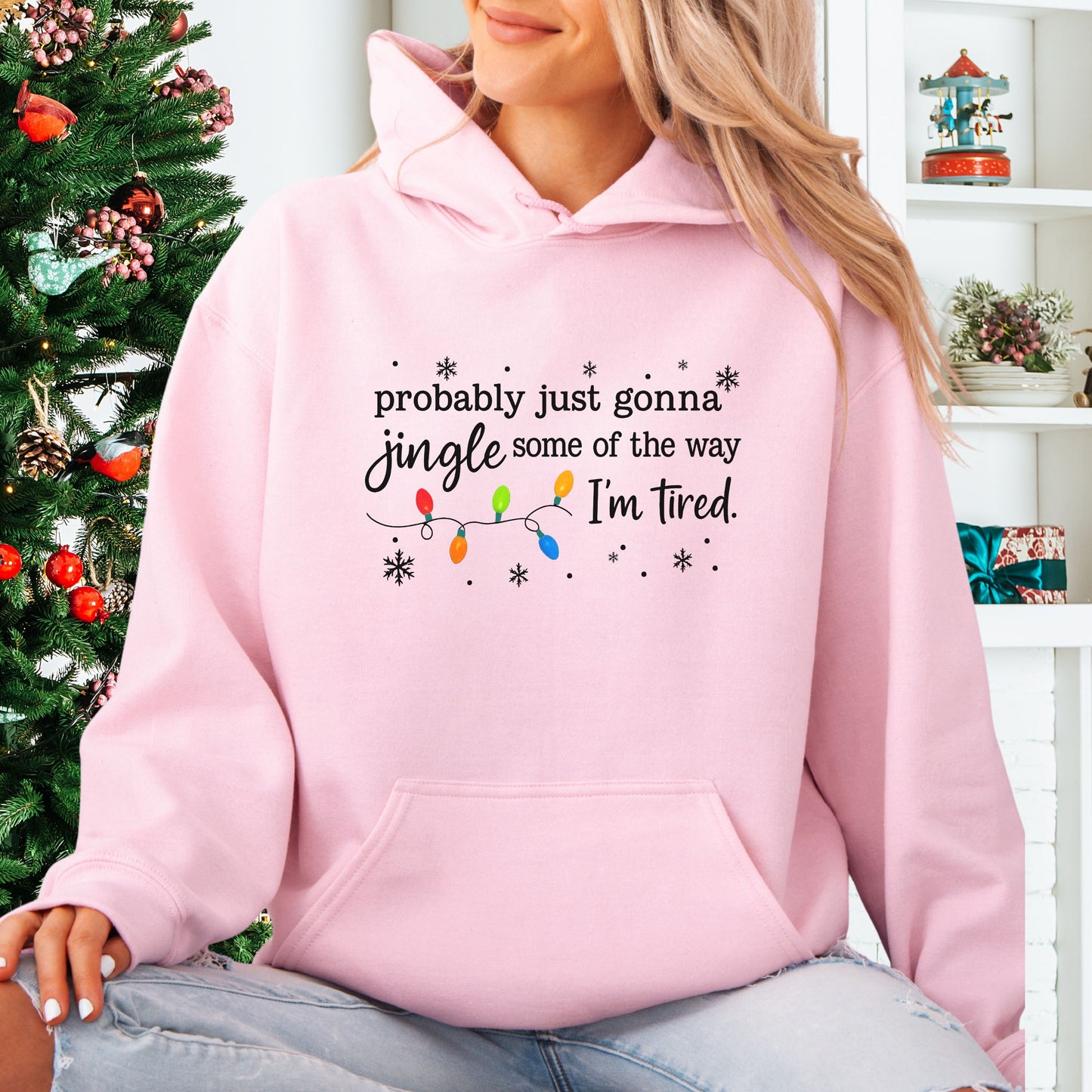 Person wearing a pink hoodie with Christmas lights and the text "probably just gonna jingle some of the way. I'm tired".