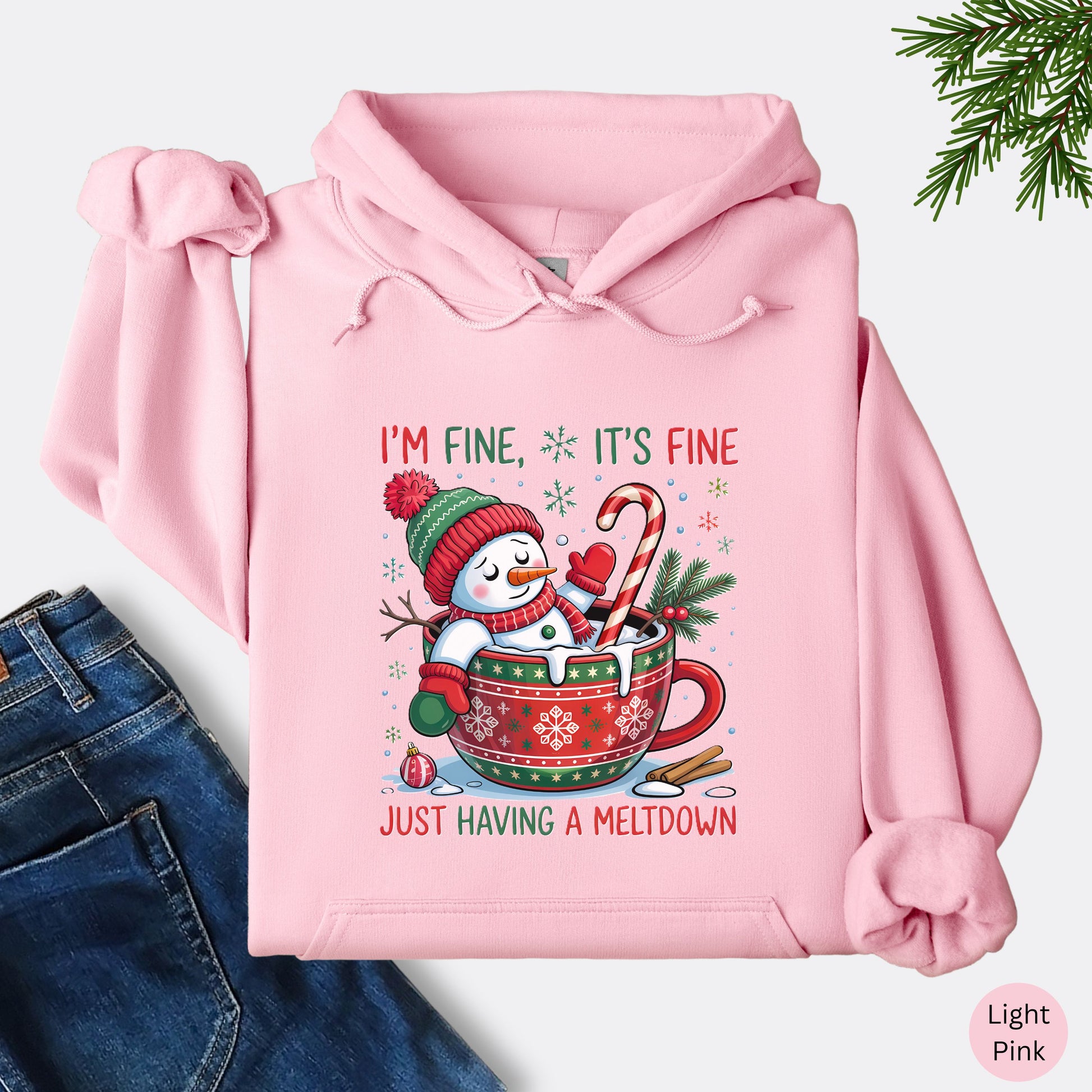 Snowman Christmas hoodie in the color light pink with festive mug design and text that reads I’m Fine It’s Fine Just Having a Meltdown.