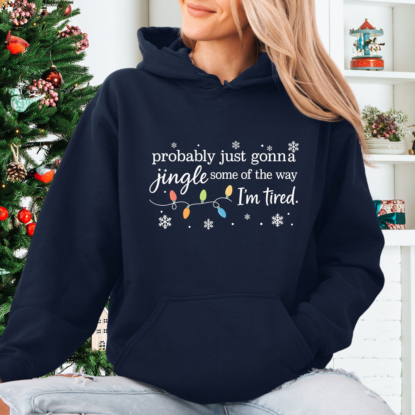Person wearing navy hoodie with Christmas lights and the text "probably just gonna jingle some of the way. I'm tired".