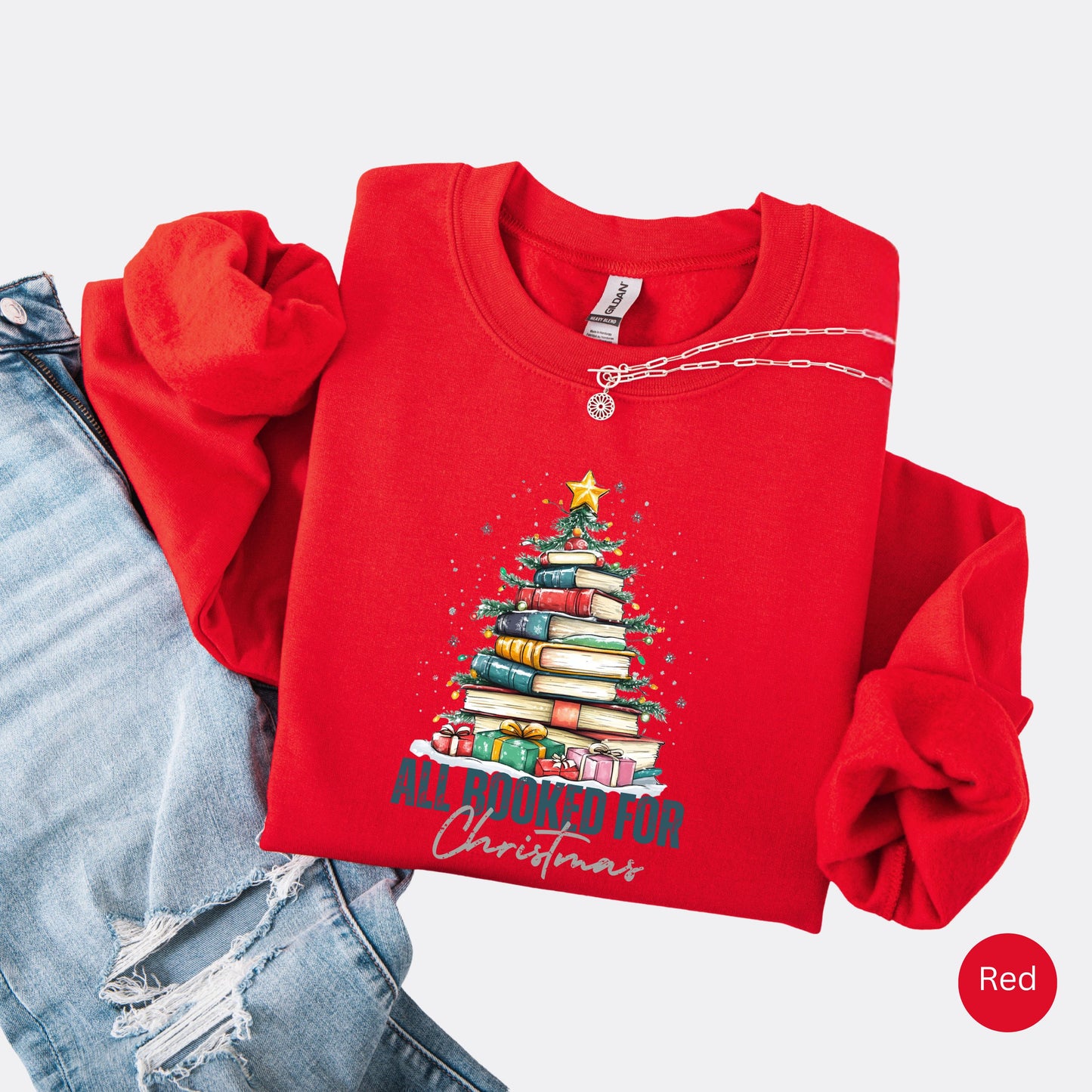 Red crewneck sweatshirt with a holiday design featuring a Christmas tree made of books and the phrase “All Booked For Christmas.”