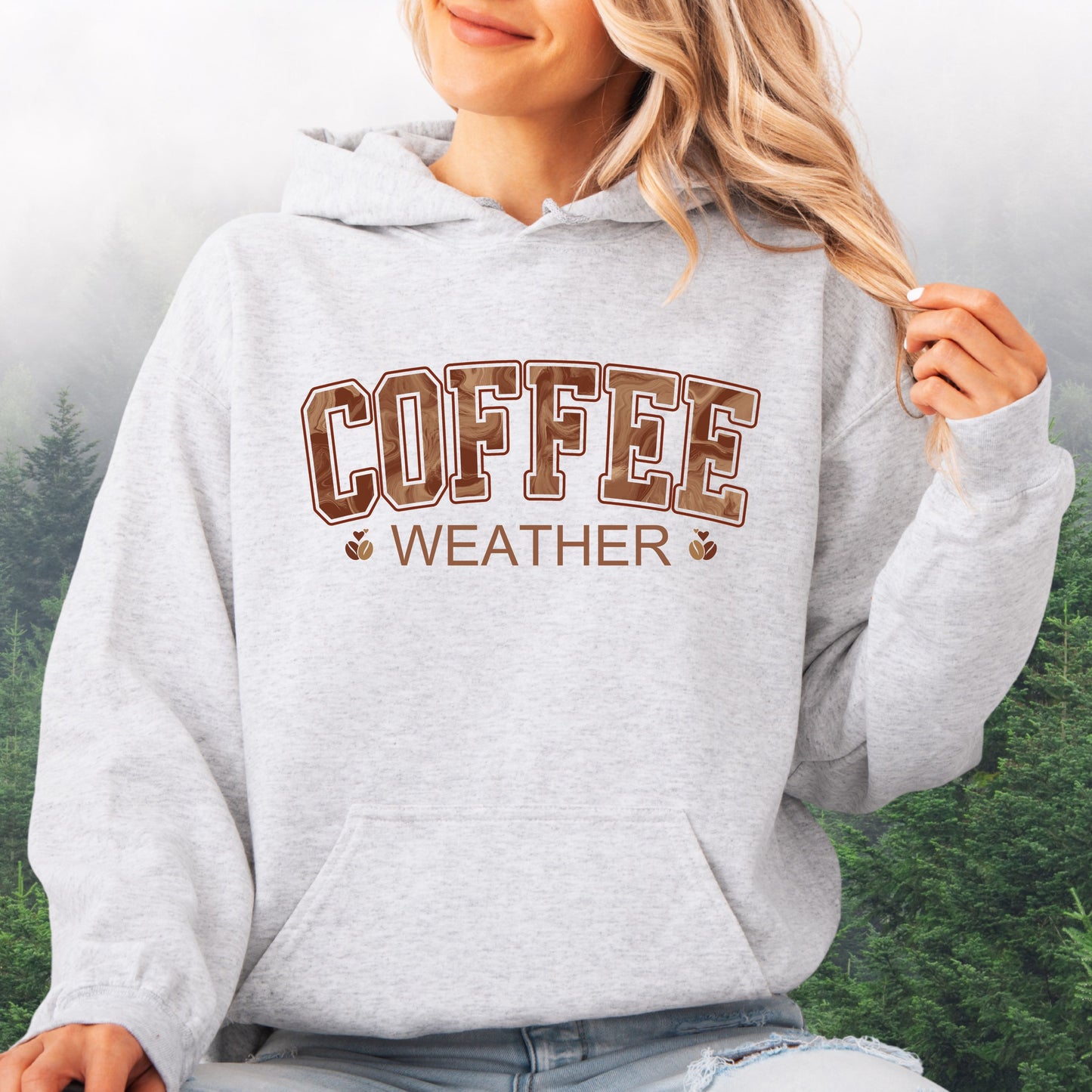 Person wearing ash colored coffee weather hoodie with marbled brown lettering and coffee bean icons.
