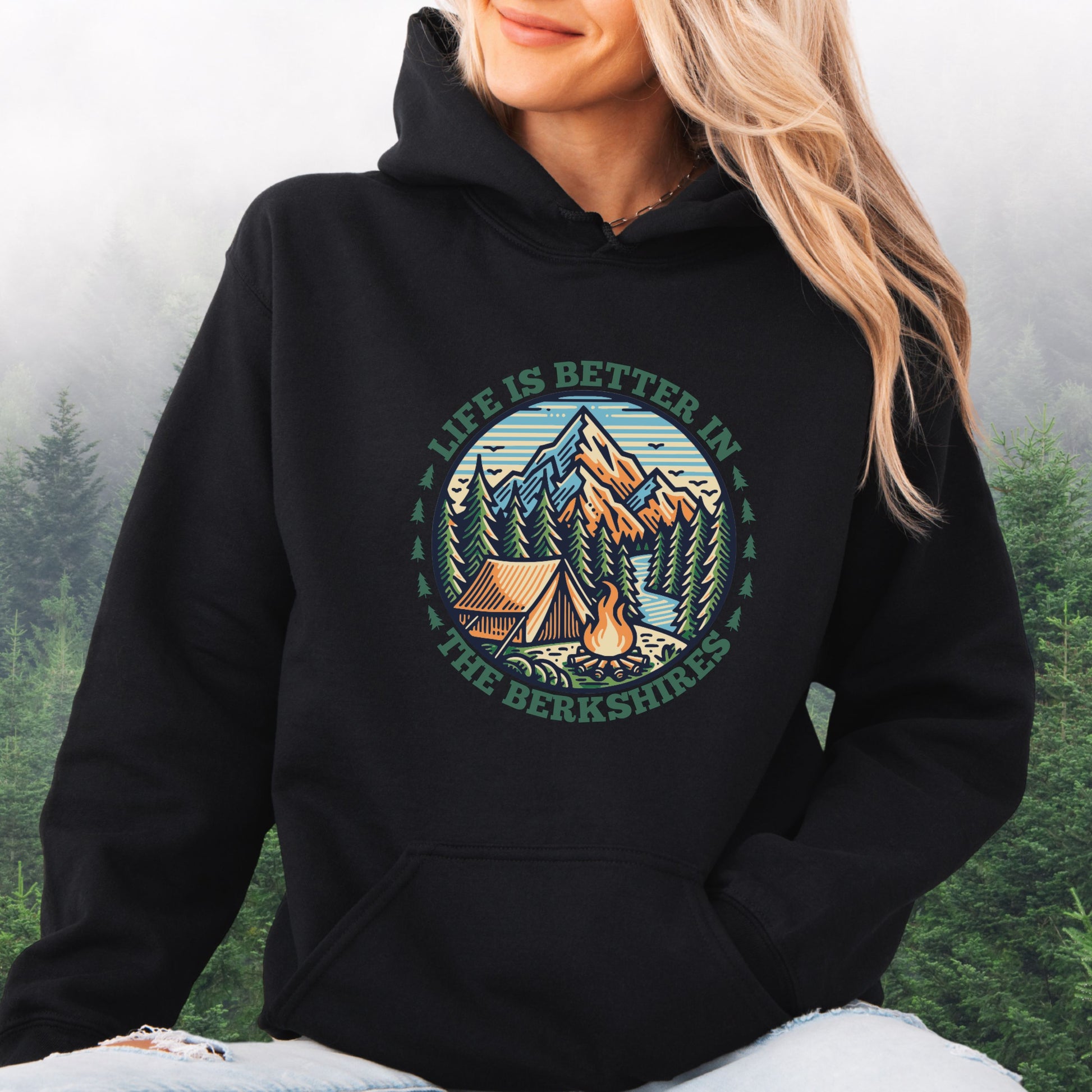 Person wearing black Hoodie with mountain scene, pine trees, tent, and campfire graphic with the text Life is Better in the Berkshires
