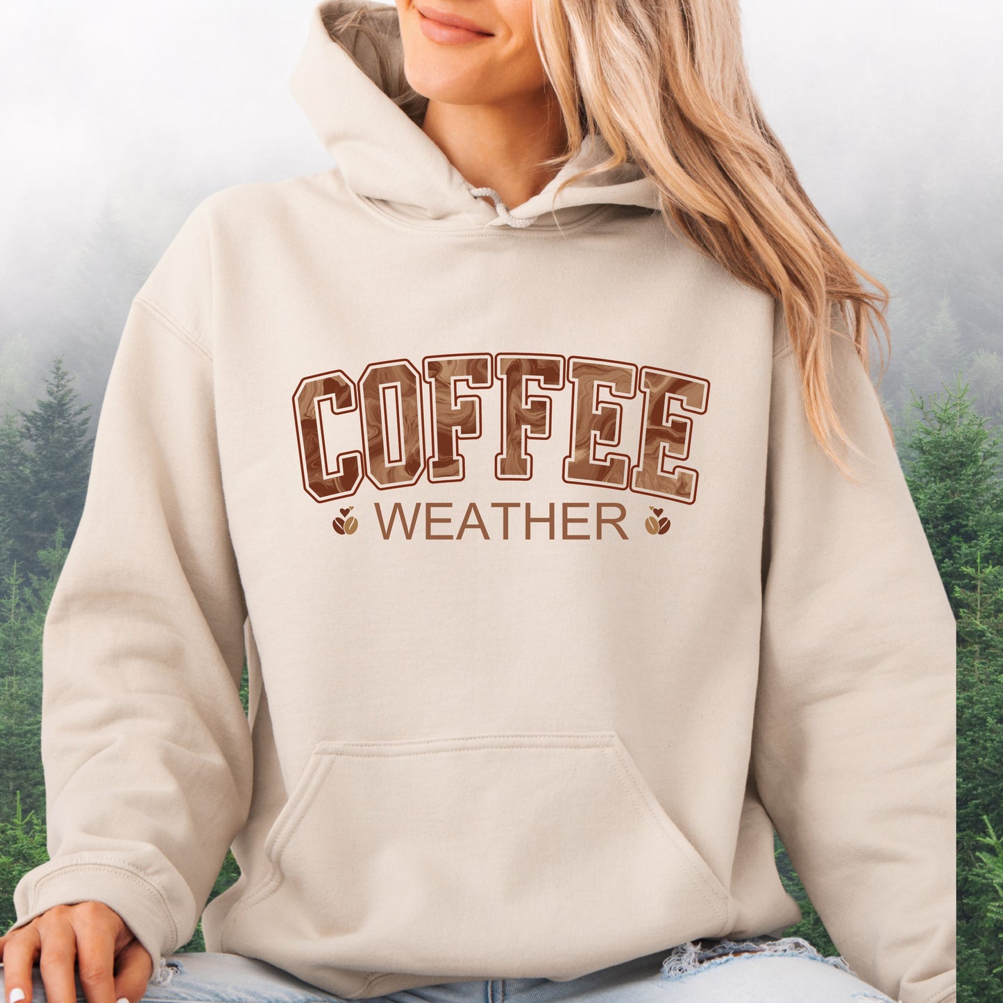 Person wearing sand  colored coffee weather hoodie with marbled brown lettering and coffee bean icons.