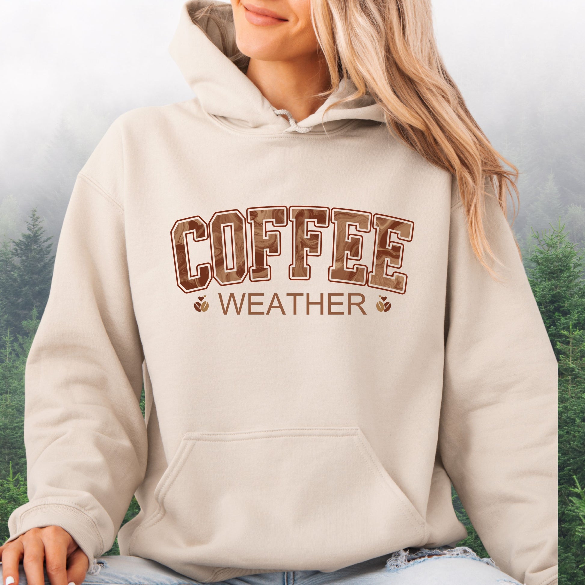 Person wearing sand  colored coffee weather hoodie with marbled brown lettering and coffee bean icons.