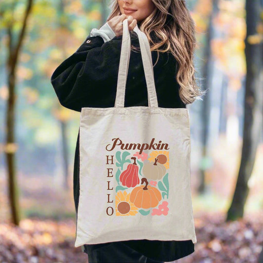 Canvas tote bag over shoulder, printed with pumpkins, sunflowers, and the phrase “Hello Pumpkin” in fall-themed colors.