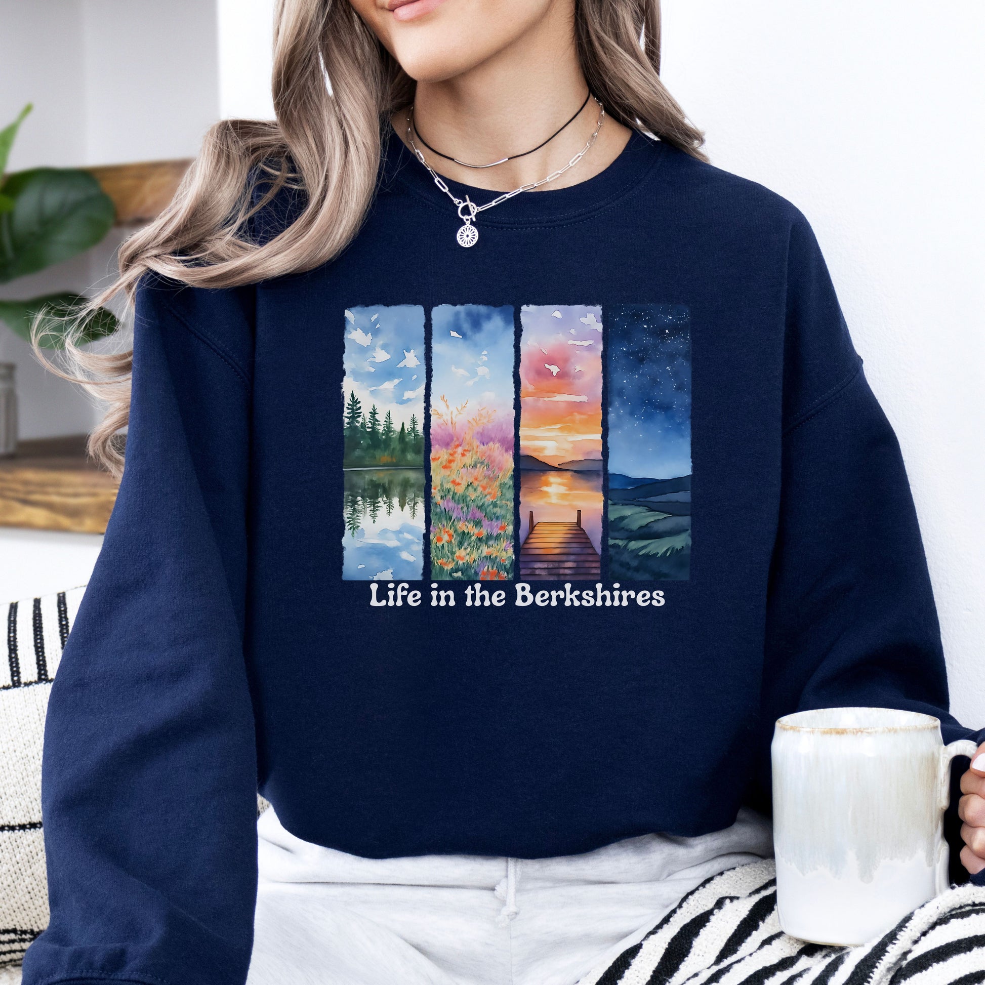 Person wearing a Navy Blue sweatshirt with 'Life in the Berkshires' design featuring four scenic panels of a lake, flowers, sunset, night sky
