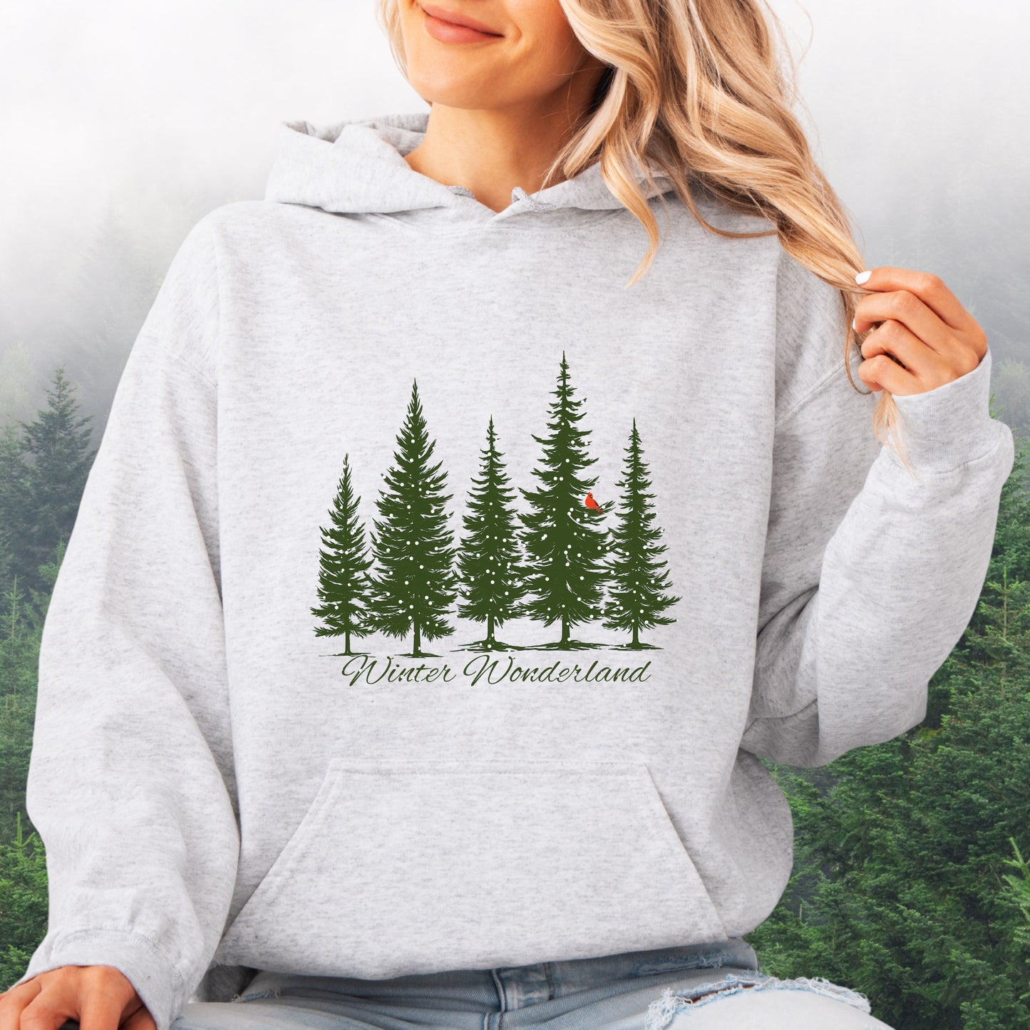 Person wearing snowy pine trees and red cardinal design on cozy unisex winter hoodie in the color ash