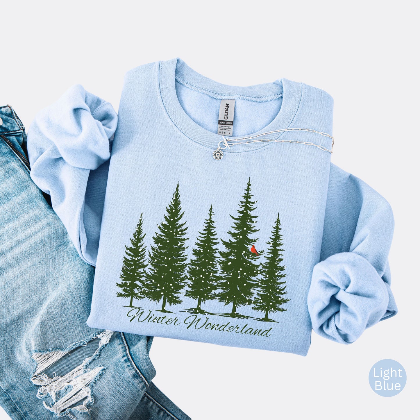 Snow covered evergreen trees with red cardinal design on light blue sweatshirt with Winter Wonderland text
