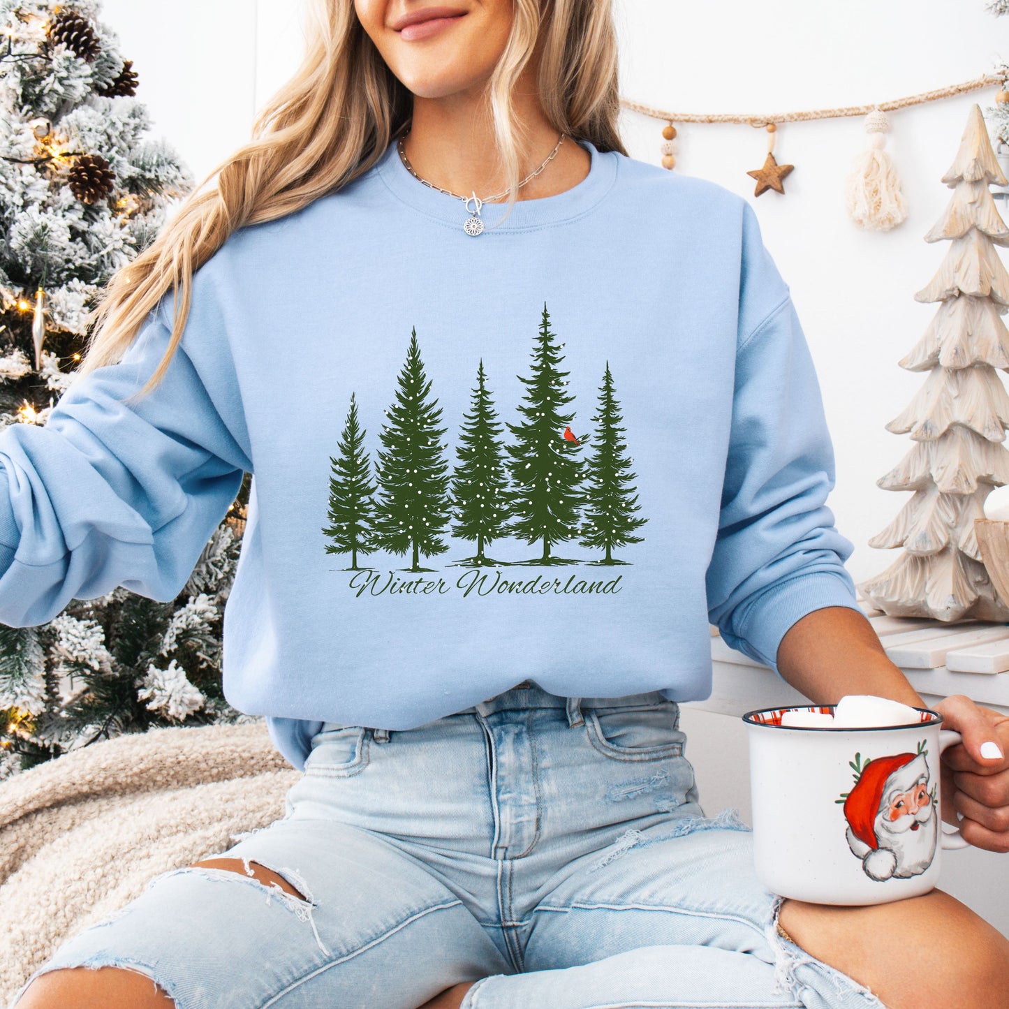 Person wearing snow covered evergreen trees with red cardinal design on light blue sweatshirt with Winter Wonderland text