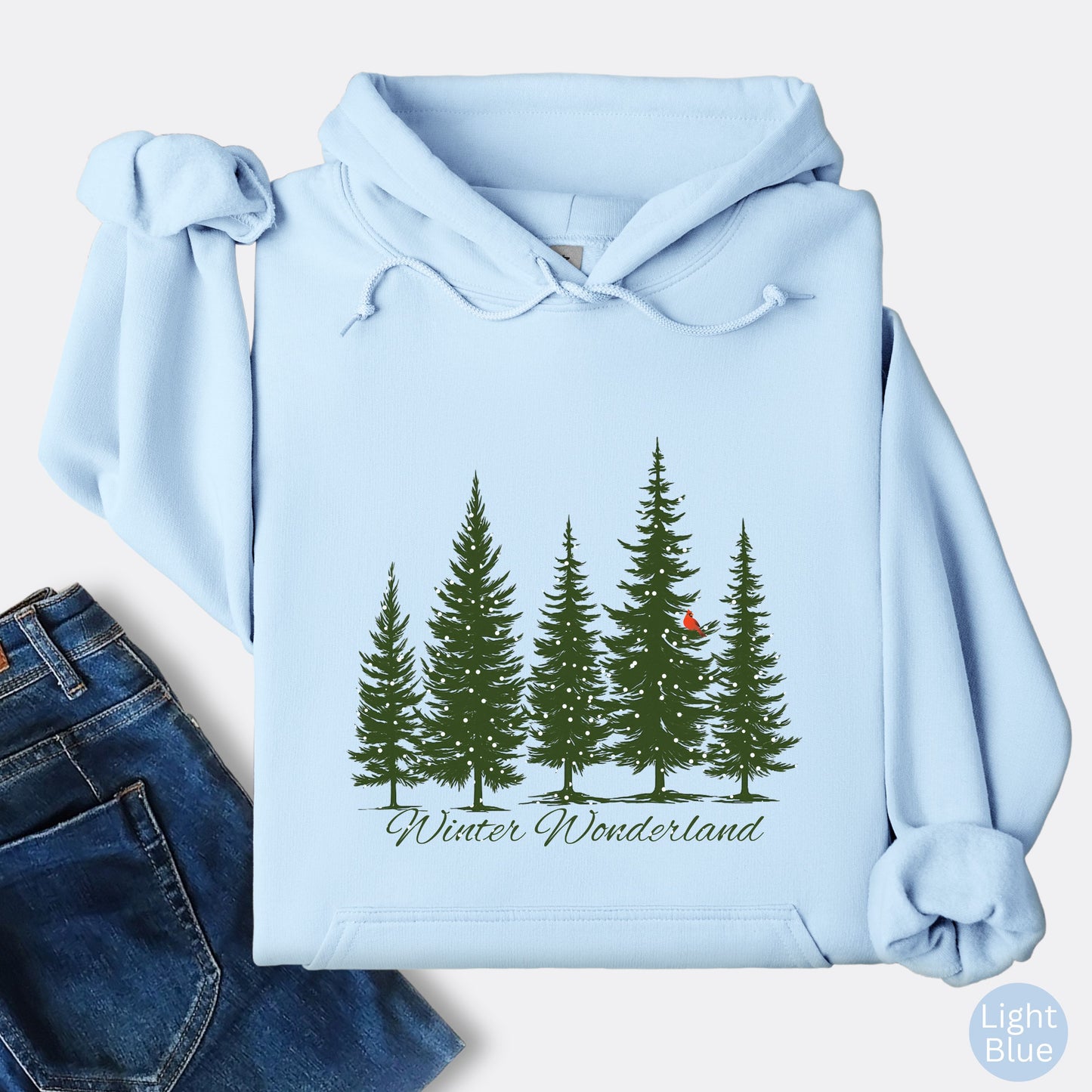 Snowy pine trees and red cardinal design on cozy unisex winter hoodie in the color light blue