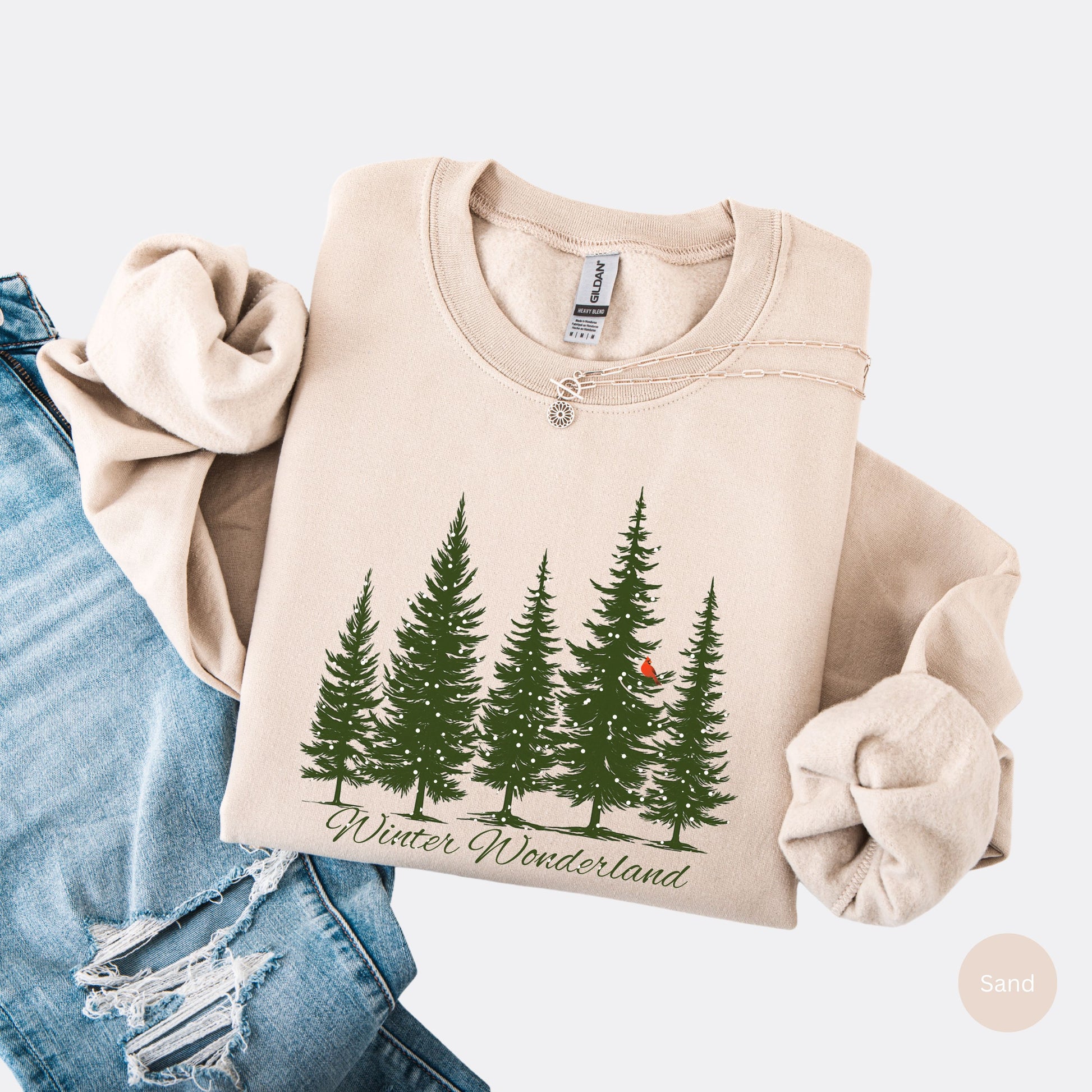 Snow covered evergreen trees with red cardinal design on sand colored sweatshirt with Winter Wonderland text