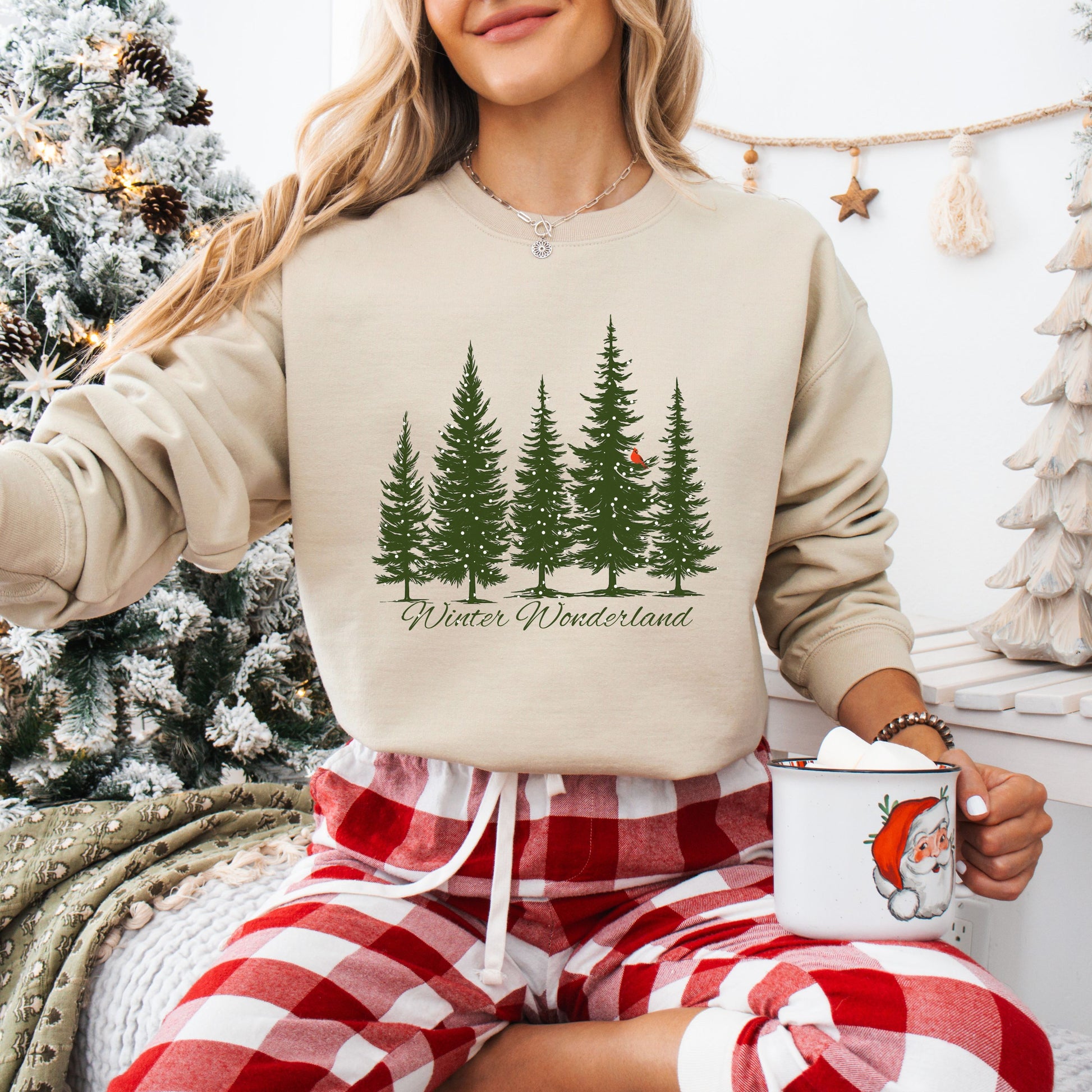 Person wearing snow covered evergreen trees with red cardinal design on sand colored sweatshirt with Winter Wonderland text