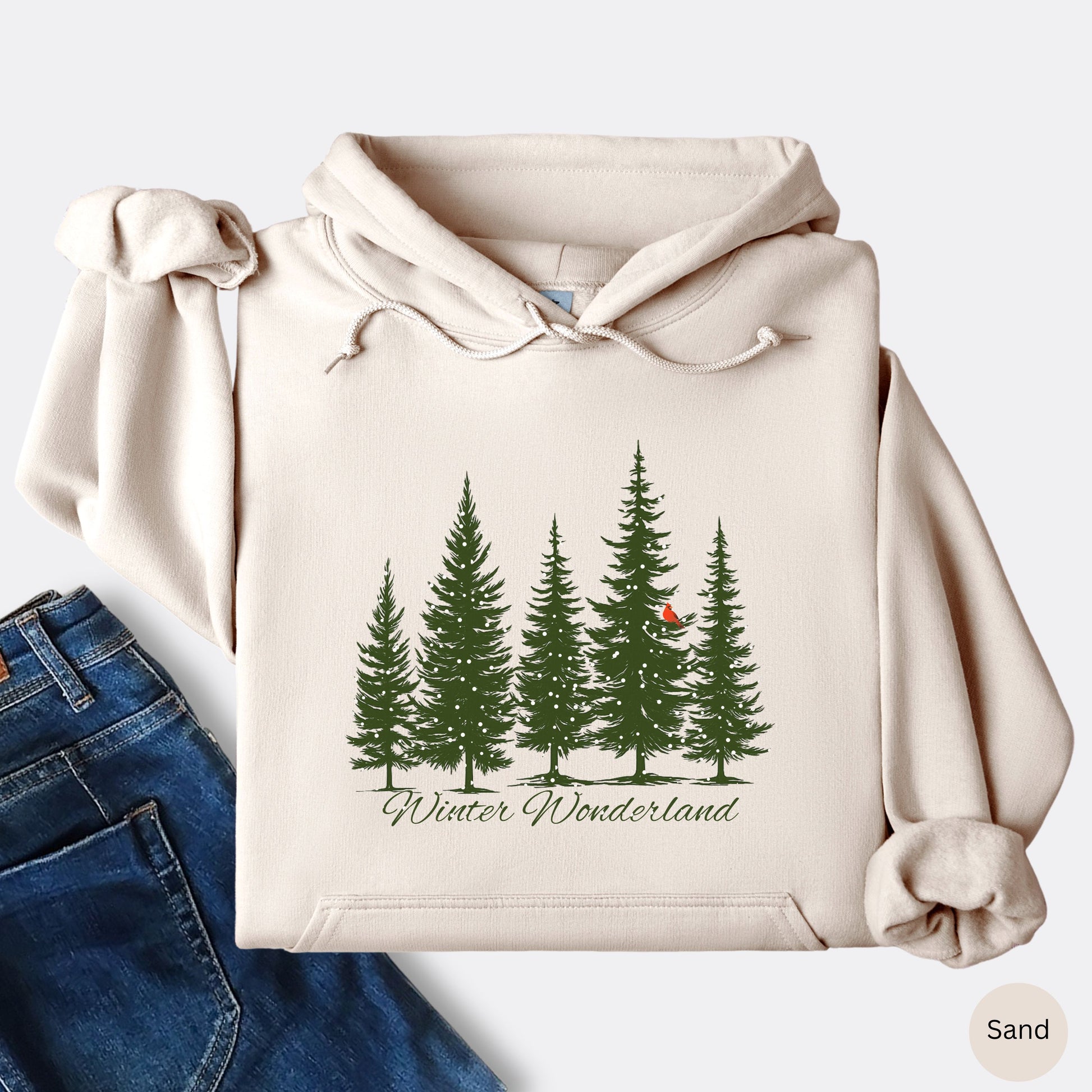 Snowy pine trees and red cardinal design on cozy unisex winter hoodie in the color sand