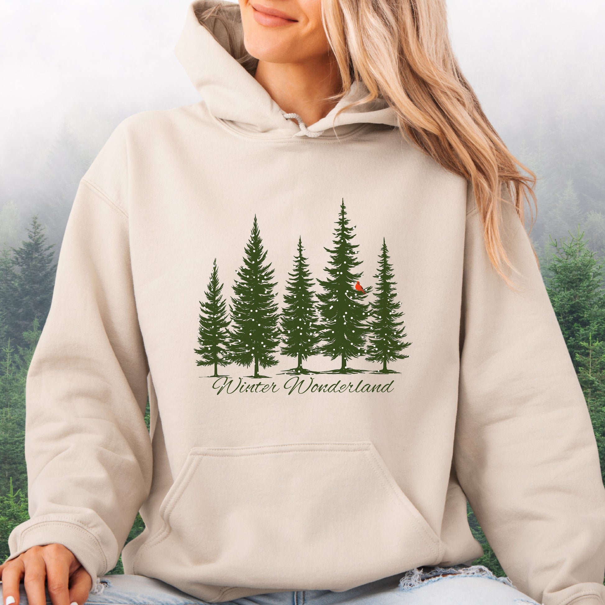 Person wearing snowy pine trees and red cardinal design on cozy unisex winter hoodie in the color sand